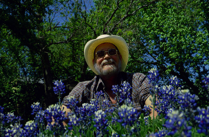 Man in a hat sitting behind a cluster of bluebonnets