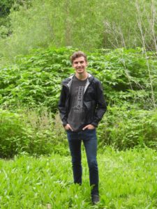 Student standing in front of bright green foliage.