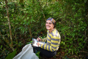 Student doing field work in a field of tall green plants.