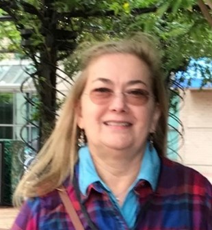 Headshot of person with long hair, glasses, plaid shirt with blue color, smiling at camera.