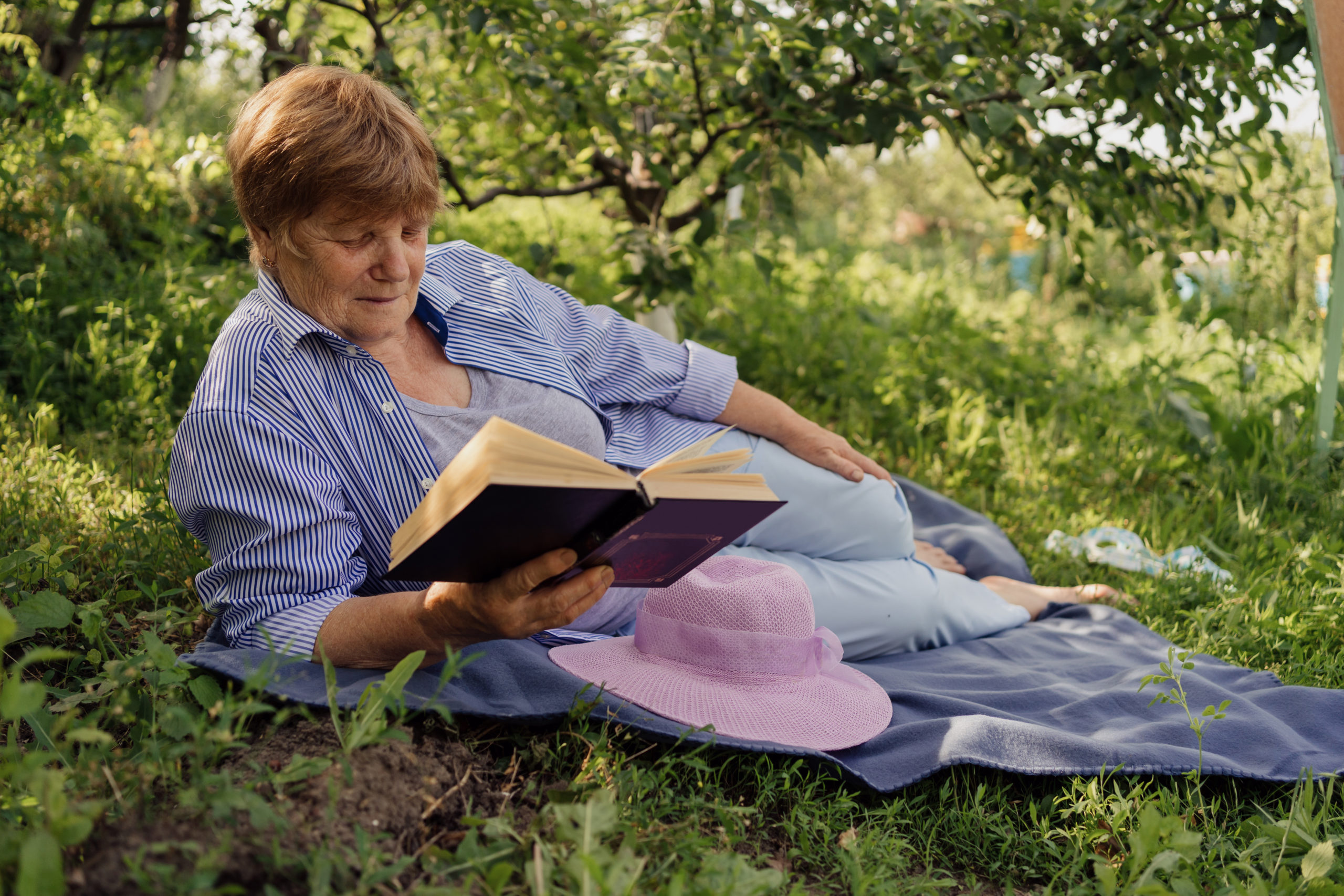 Woman lounging outside under a tree, reading a book.