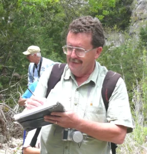 A person standing outdoors, holding a notebook, writing notes.