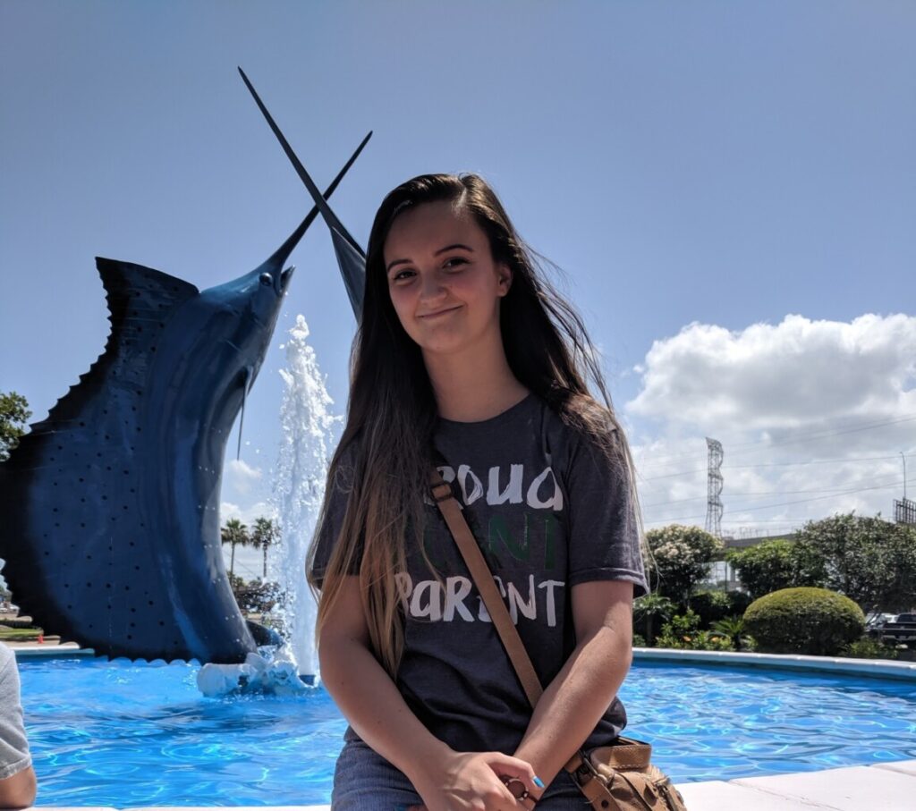 Image of young person sitting next to a fountain with a statue of sword fish