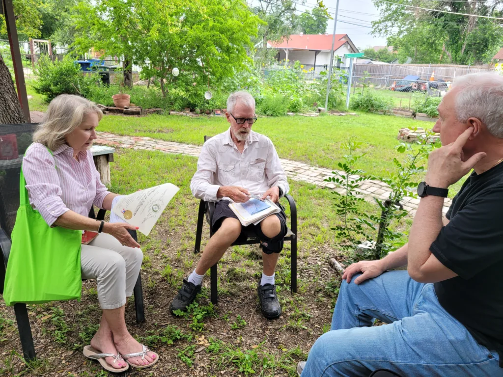 Three people sitting in lawn chairs in a back yard surrounded by native plants.