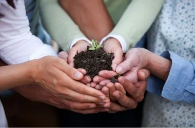 Group of people of all ages holding a plant in soil