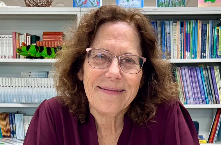 A person positioned in front of bookshelves filled with books and decorative items.